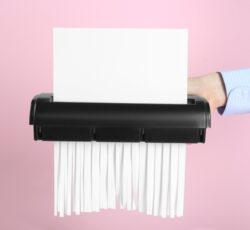 Woman,destroying,sheet,of,paper,with,shredder,on,pink,background,